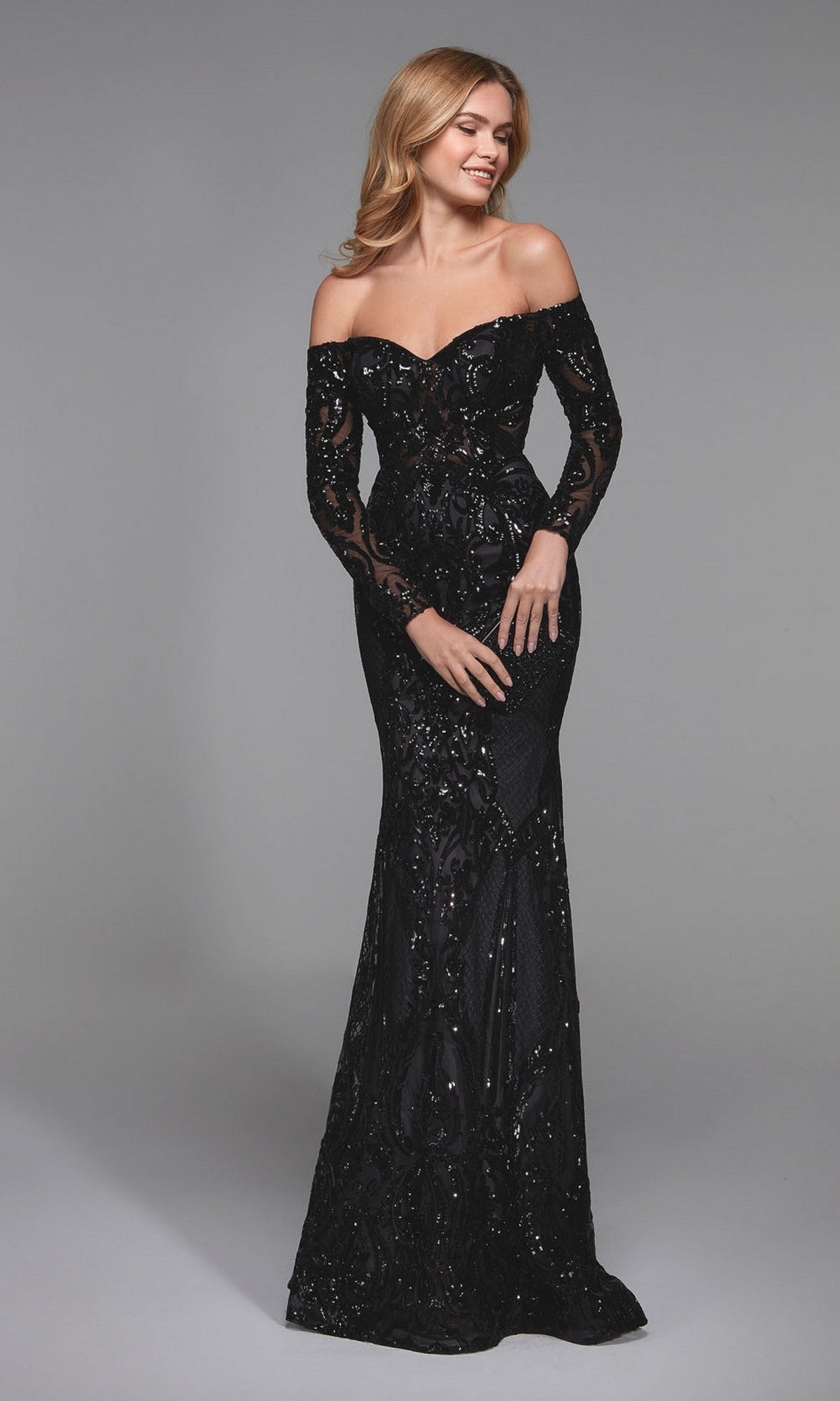 A woman poses against a plain gray background wearing the black Alyce 27544, a long formal dress featuring off-the-shoulder long sleeves, sequin detailing, a fitted bodice, and a floor-length skirt.
